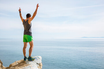 Runner raising arms in victory on protruding rock, Santa Barbara, California, USA