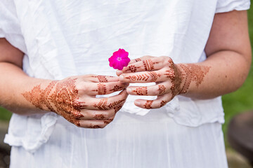Woman in white dress with henna tattoo on hands holding flower