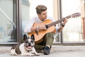 Teenage refugee boy playing guitar on pavement with dog
