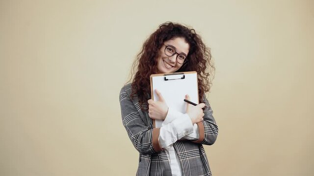 Smiling businesswoman holds in her hand a business plan and satisfied smiles wide. Cretaceous in gray jacket and white shirt, with glasses posing isolated on a beige background in the studio. The