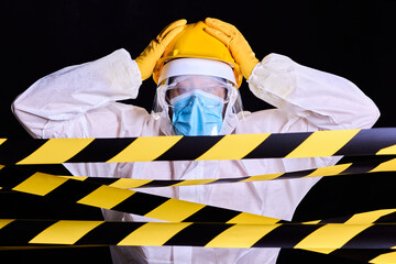 Fototapeta premium Health worker for corona virus pandemic, surrounded by security tapes, hands on his helmet in amazement, on solid black background