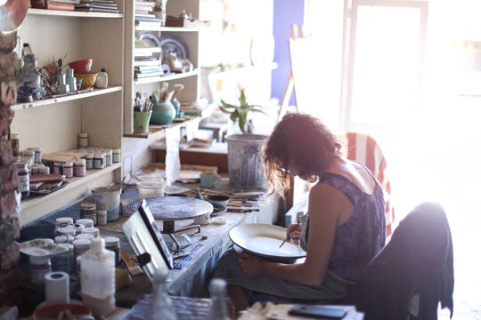 Female potter painting ceramic plate in workshop