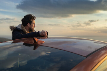 Man resting against car on roadside, enjoying view on hilltop
