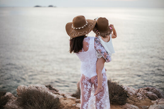 Mother carrying toddler son looking out to sea, rear view, Santa Teresa Gallura, Sardinia, Italy