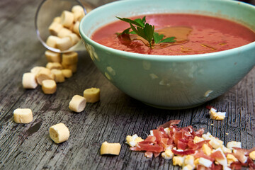 Close-up view of Andalusian gazpacho bowl with parsley and extra virgin olive oil, accompanied by croutons, Serrano ham and chopped boiled egg. Concept of mediterranean food, healthy.