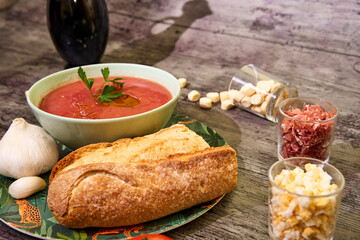 Gazpacho in a bowl with parsley. Accompanied by bread and garlic, and on the right are croutons, Serrano ham and egg. At the back the shadow of olive oil bottle. Concept of mediterranean food, healthy