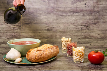 Extra virgin olive oil being served with Andalusian gazpacho in a bowl. Accompanied by bread and garlic, and on the right are croutons, egg and Serrano ham, and a tomato. Concept of mediterranean food