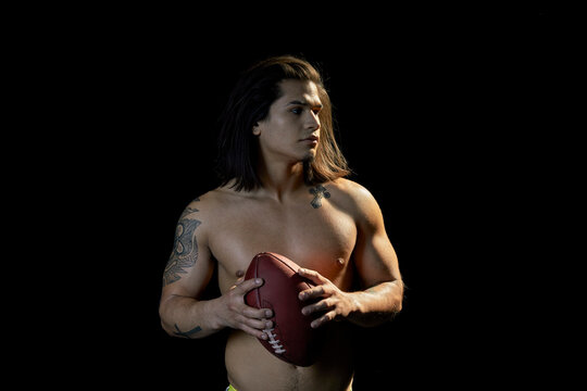 Portrait of bare chested young man with football, black background