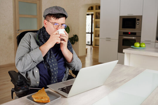 Physically impaired man drinking and working on laptop at home