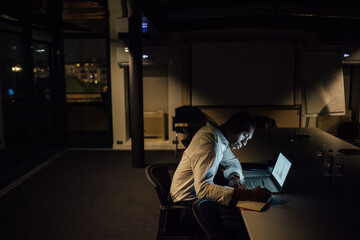 Young businessman in office at night making notes from laptop