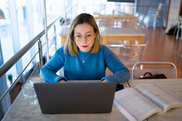 Female higher education student typing on laptop in university cafe