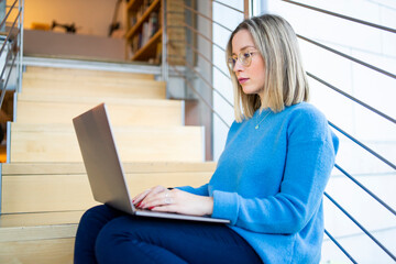 Female higher education student sitting on university stairway typing on laptop