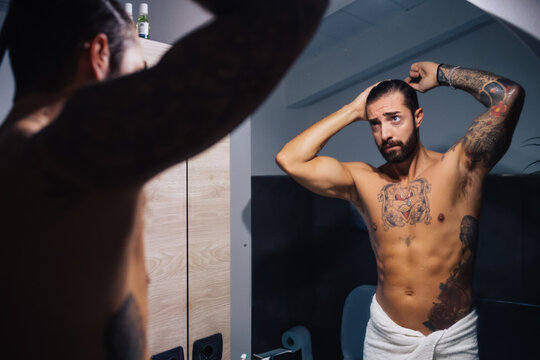 Mid adult man with tattoos combing hair at bathroom mirror, mirror image