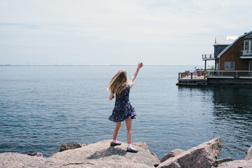 Blond haired girl waving from lakeside, rear view, Kingston, Ontario, Canada