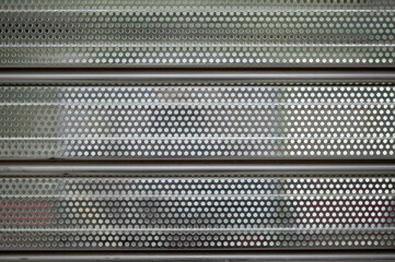 gray metal shutter of a store or establishment with many holes