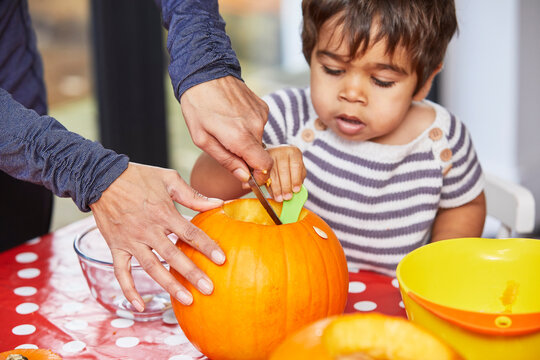 Boy helping mother gut pumpkin in kitchen