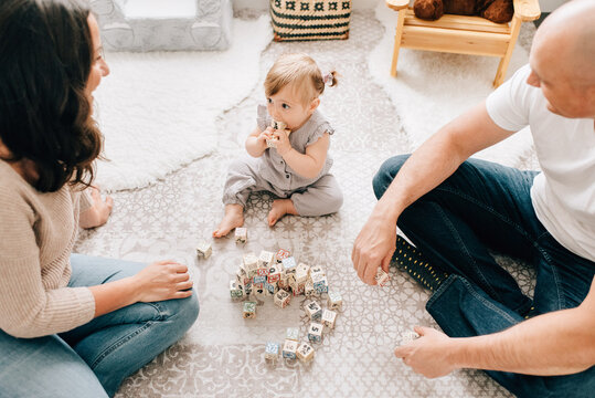 Mother and father sitting on nursery floor with baby daughter playing with building blocks