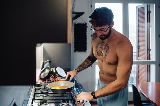 Mid adult man with tattooed chest using gas hob