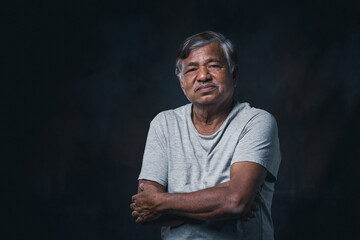 Portrait elderly Asian man with crossed arms on black background in the studio.