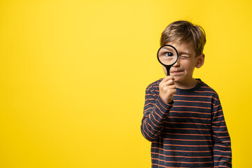 Front view portrait of small caucasian boy curious child holding a magnifying glass for reading in...