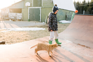 Boy with cat looking at farmyard skateboard ramp
