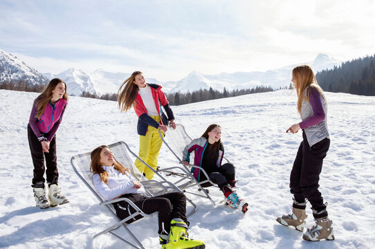 Five teenage girl skiers standing and in deck chairs in snow covered landscape, Tyrol, Styria, Austria