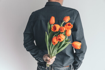 Handsome man with a bouquet of orange tulips behind his back. Surprise for your beloved woman. Romantic holiday concept.
