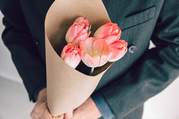 Elegant man holding bouquet of pink tulips wrapped in craft paper.Surprise for your beloved woman.Romantic getaway concept
