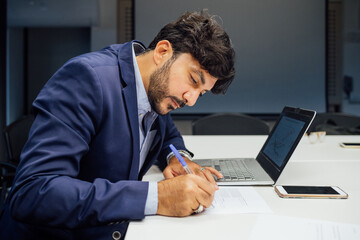 Businessman writing notes and using laptop in office