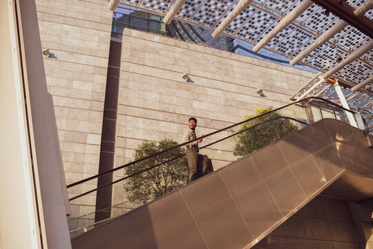 Businessman ascending escalator of office building, Milano, Lombardia, Italy - Powered by Adobe