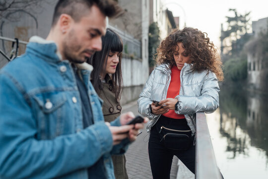 Friends using smartphone by river, Milano, Lombardia, Italy