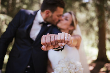 Romantic bride and groom kissing and showing wedding rings in woodland, selective focus on hands