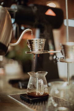 Boiled kettle water pouring into coffee filter and dripping into jug on cafe counter, shallow focus