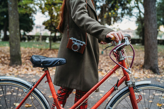 Young woman pushing bicycle in autumn park, neck down