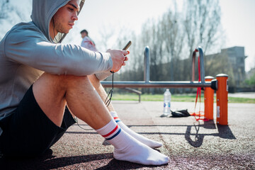 Calisthenics class at outdoor gym, young man sitting down and looking at smartphone