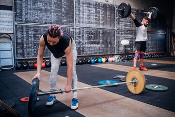 Young woman placing weight plate into bar in gym