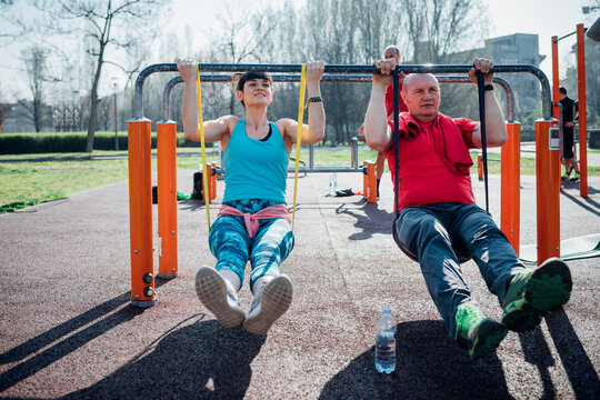 Calisthenics class at outdoor gym, mature man and young woman exercising on parallel bars