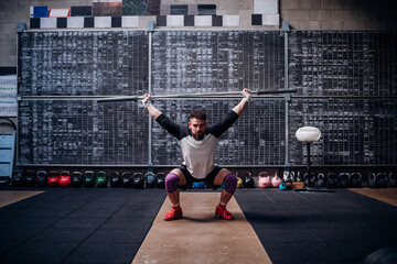 Young man lifting weight bar in gym