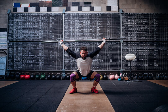Young man lifting weight bar in gym