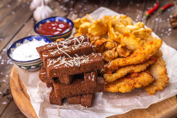 Rye croutons, crab meat in batter and a set of sauces on a wooden stand.