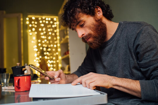 Bearded young man using smartphone and reading at home