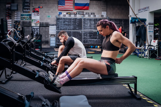 Young woman and man training together, preparing to use rowing machines in gym