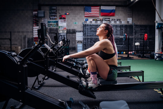 Young woman and man training on rowing machines together in gym, side view
