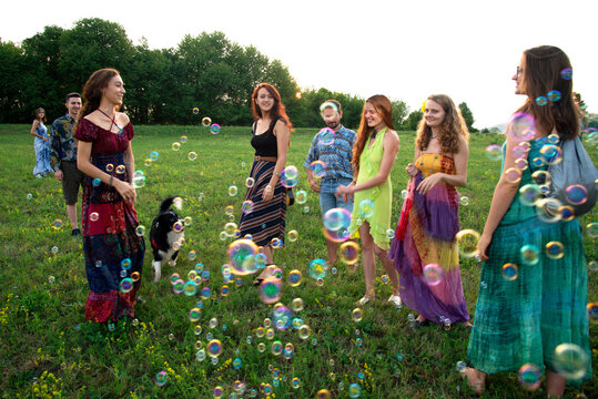 Large group of happy young adults standing in field with floating bubbles