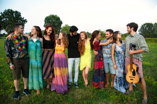 Large group of happy young adults standing in field with arms around each other