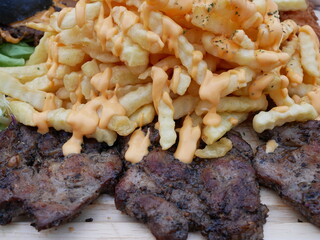 beef steak grilled and french fries on a wooden plate.