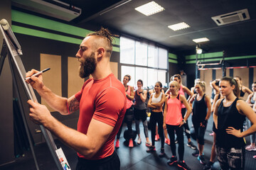Group of women training in gym, watching male trainer writing on flip chart