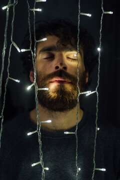 Bearded young man standing between strings of decorative lights