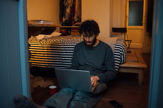 Bearded young man using laptop in bedroom