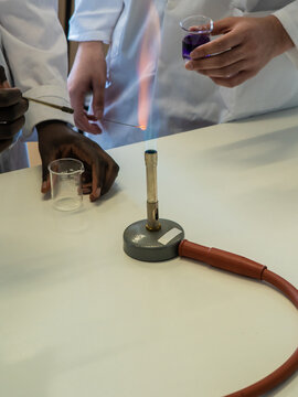 Young female and male scientists experimenting with liquid and bunsen burner in laboratory, cropped